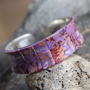May include: A purple, pink, and gold patterned polymer clay bracelet with a silver metal band.