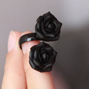 Puede incluir: Un anillo negro con dos acentos de rosas negras. El anillo está hecho de un material negro brillante y las rosas están hechas de un material negro mate.