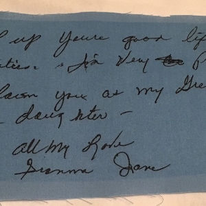 May include: A handwritten note on a blue fabric patch. The black ink script reads, "Keep up your good life and activities. I'm very proud to claim you as my Great Grand daughter - all my love, Dianna Jane."