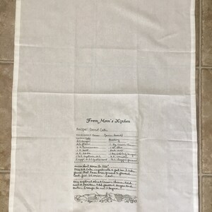 May include: A white kitchen towel with a handwritten recipe for carrot cake. The recipe includes ingredients like carrots, sugar, flour, and spices. The towel also features a small illustration of kitchen tools.