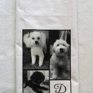May include: White kitchen towel with a black and white photo collage of three dogs. The dogs are a white poodle, a white fluffy dog, and a black poodle. The letter "D" is printed in a cursive font in the bottom right corner of the towel.