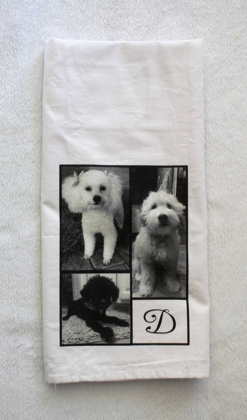 May include: White kitchen towel with a black and white photo collage of three dogs. The dogs are a white poodle, a white fluffy dog, and a black poodle. The letter "D" is printed in a cursive font in the bottom right corner of the towel.