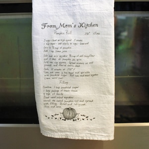 May include: A white tea towel with handwritten instructions for making a pumpkin roll. The instructions include ingredients and steps for both the pumpkin roll and the filling. The text reads "From Mom's Kitchen Pumpkin Roll 350&deg; 15 mins".