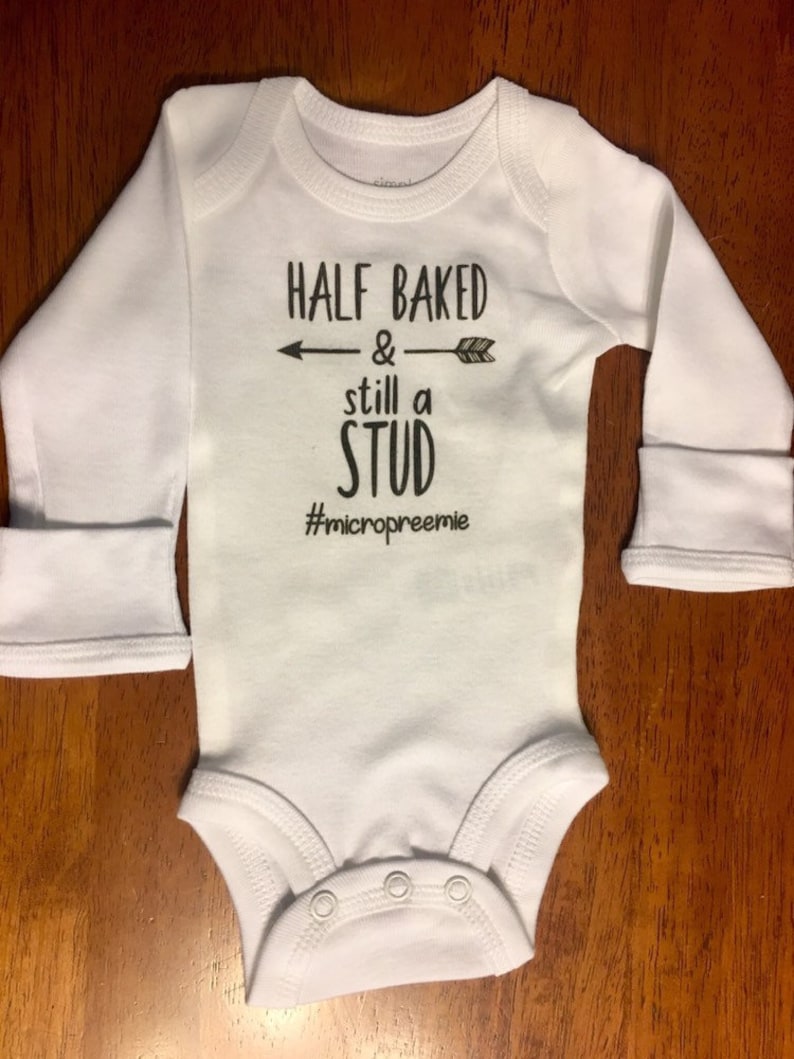 May include: White long-sleeve baby onesie with black text that reads "Half Baked & still a stud #micropreemie".
