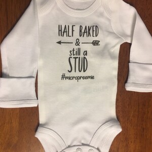 May include: White long-sleeve baby onesie with black text that reads "Half Baked & still a Stud #micropreemie".