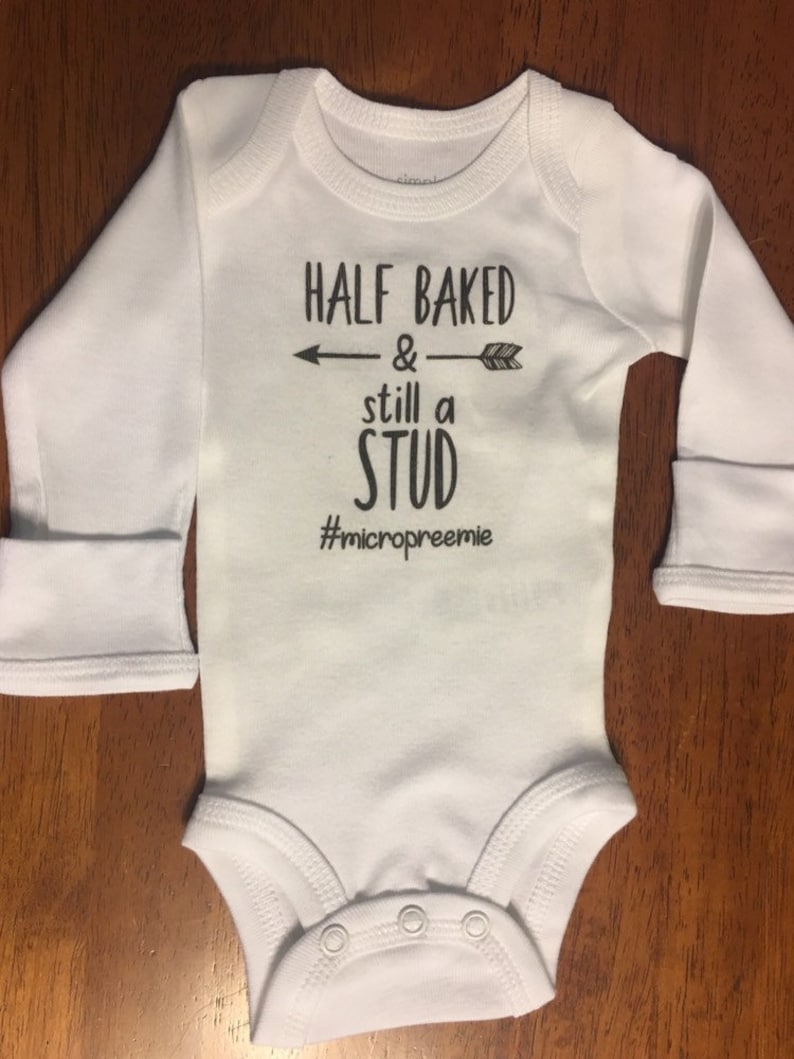 May include: White long-sleeve baby onesie with black text that reads "Half Baked & still a Stud #micropreemie".