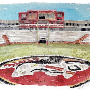 May include: A watercolor painting of a football stadium with a scoreboard displaying "FSU 19:29". The stadium is called "Bobby Bowden Field at Doak Campbell Stadium". The painting also includes the text "1999 National Cha" and "AL Champions".