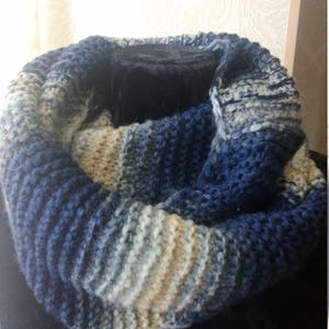 以下が含まれることがあります： 青、白、ベージュのニットのインフィニティスカーフ。スカーフは柔らかく厚手の糸でできており、質感のあるリブ模様になっています。
