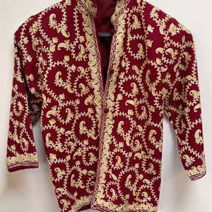 Peut inclure: Une veste brodée de couleur bordeaux avec un motif cachemire doré. La veste a un col mandarin et une fermeture à bouton.