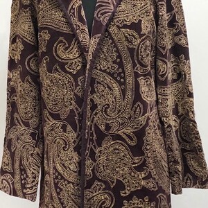 Op de afbeelding: Een lange bruine fluwelen jas met een gouden paisley-patroon.