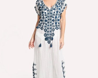 May include: White maxi dress with intricate navy blue embroidery. The dress features a V-neckline, short sleeves, and decorative tassels. The embroidery design is repeated along the hemline and sleeves, creating a cohesive look. The dress is made of a lightweight fabric.
