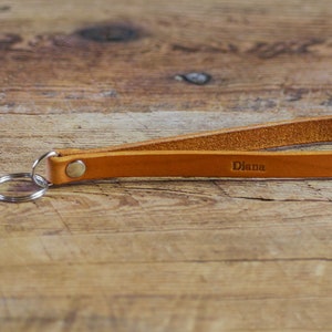 May include: A tan leather keyring with a silver key ring and a brass snap. The keyring is personalised with the name "Diana" embossed on the leather.