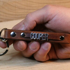 May include: Brown leather keychain with silver metal accents and the name "COOPER" engraved on it.