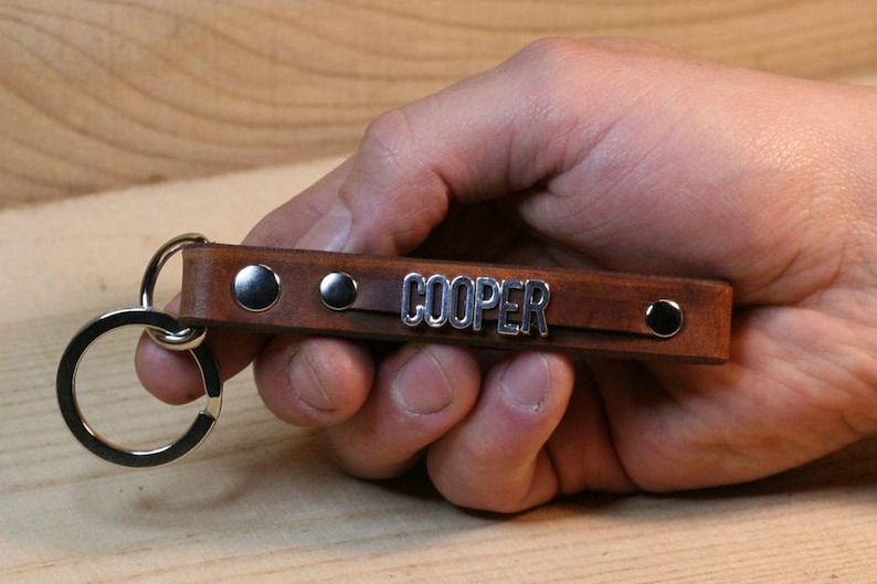 May include: Brown leather keychain with silver metal accents and the name "COOPER" engraved on it.