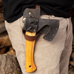 May include: A brown leather sheath with a wood-handled axe attached to a belt. The axe has a black metal head and a brown leather strap.