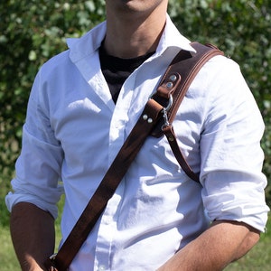 May include: A white button-down shirt with a brown leather camera strap. The strap has a silver buckle and a silver ring.