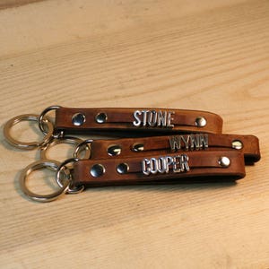 May include: Three brown leather keychains with silver metal name tags. The names on the tags are Stone, Wynn, and Cooper.
