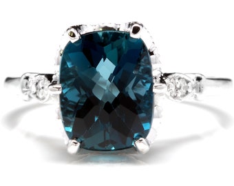 Può includere: Un anello d'argento con un grande topazio blu a cuscino circondato da un'aureola di diamanti più piccoli.