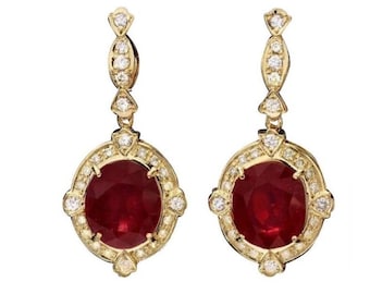 Puede incluir: Un par de pendientes de oro con una gran piedra de rubí ovalada rodeada de diamantes más pequeños. Los pendientes tienen un diseño delicado y colgante.