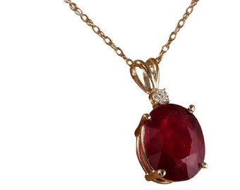 Op de afbeelding: Een gouden ketting met een hanger met een grote ovale robijn en een kleinere diamant accent.