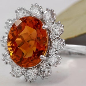 May include: A gold ring featuring a large orange gemstone encircled by a halo of smaller diamonds.