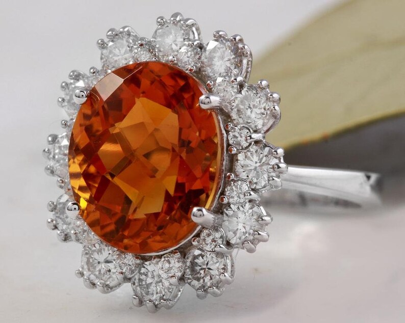 May include: A gold ring featuring a large orange gemstone encircled by a halo of smaller diamonds.