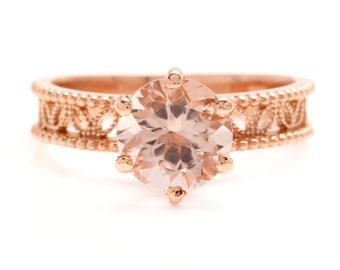 May include: A rose gold ring with a delicate filigree band and a large, round, pale pink gemstone.