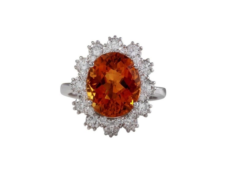May include: A silver ring featuring a large oval orange gemstone encircled by a halo of smaller diamonds.