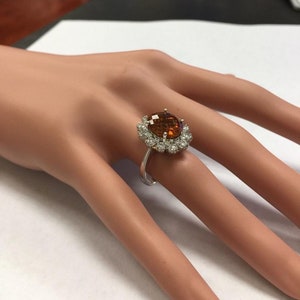 May include: A silver ring featuring a large oval brown gemstone encircled by a halo of smaller white gemstones.
