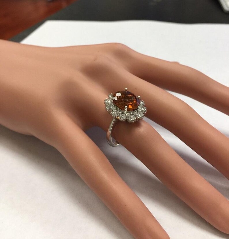 May include: A silver ring featuring a large oval brown gemstone encircled by a halo of smaller white gemstones.