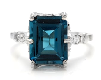 Può includere: Un anello d'argento con una grande pietra preziosa blu scuro di taglio smeraldo circondata da diamanti più piccoli.