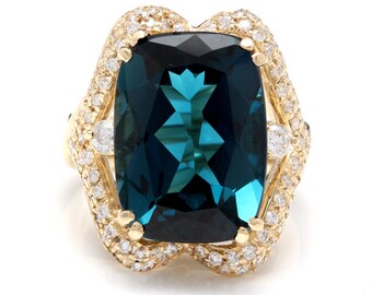 Può includere: Un anello d'oro con una grande pietra preziosa blu scuro circondata da un'aureola di diamanti più piccoli.