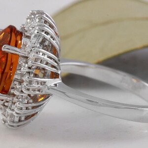 May include: A silver ring featuring a large orange gemstone encircled by smaller clear gemstones.
