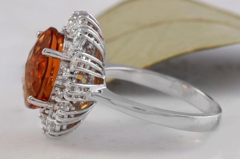 May include: A silver ring featuring a large orange gemstone encircled by smaller clear gemstones.
