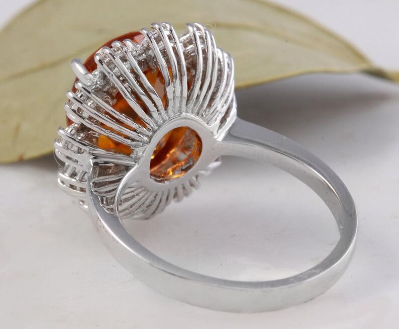May include: A silver ring featuring a large orange gemstone encircled by smaller clear gemstones. The ring is set in a halo style.