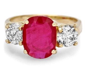 May include: A gold ring featuring a large oval ruby gemstone flanked by two smaller round diamonds.
