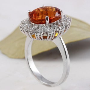 May include: A silver ring featuring a large oval orange gemstone set within a halo of smaller white gemstones.