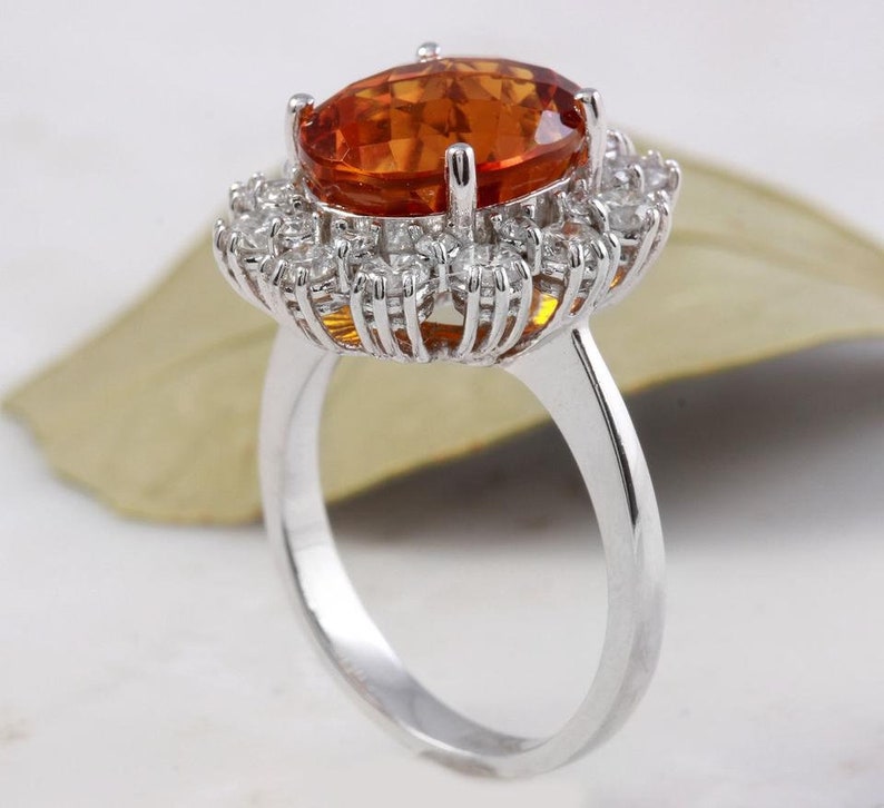 May include: A silver ring featuring a large oval orange gemstone set within a halo of smaller white gemstones.
