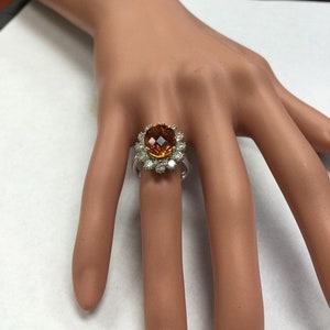 May include: A gold ring featuring a large orange gemstone encircled by smaller diamonds.