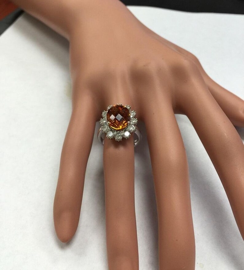May include: A gold ring featuring a large orange gemstone encircled by smaller diamonds.