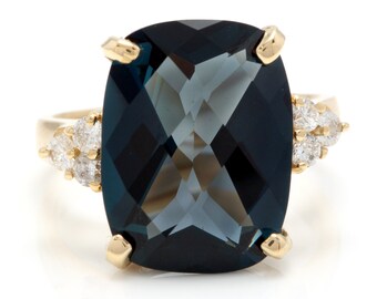Può includere: Un anello d'oro con una grande pietra preziosa blu scuro e diamanti più piccoli incastonati nella fascia.