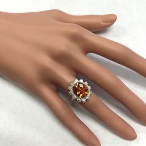 May include: A white gold ring featuring a large oval orange gemstone encircled by a halo of smaller white gemstones.