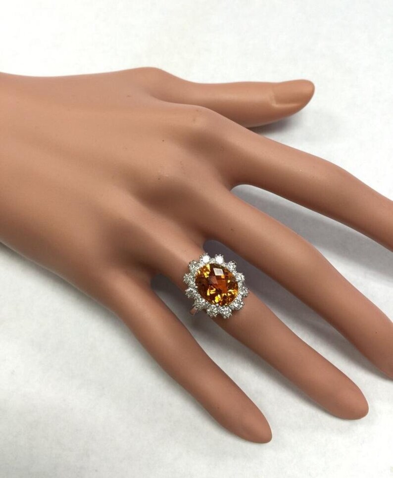 May include: A white gold ring featuring a large oval orange gemstone encircled by a halo of smaller white gemstones.