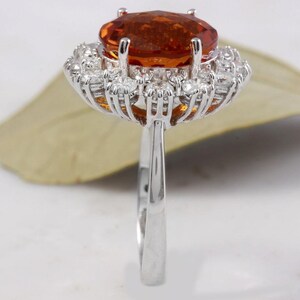 May include: A silver ring featuring a large orange gemstone encircled by a halo of smaller white gemstones.