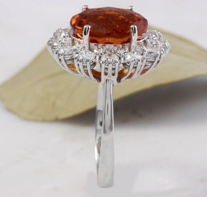 May include: A silver ring featuring a large orange gemstone encircled by a halo of smaller white gemstones.