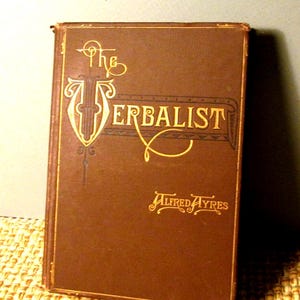 May include: A vintage hardcover book titled "The Verbalist" by Alfred Ayres. The cover is a rich brown with gold lettering and decorative elements. The book's edges show signs of wear.