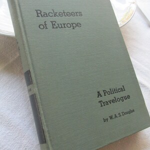 May include: A green hardcover book titled "Racketeers of Europe: A Political Travelogue by W.A.S. Douglas".