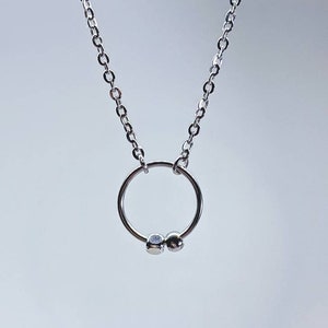 Può includere: Una collana a catena d'argento con un piccolo ciondolo circolare e due perline d'argento.