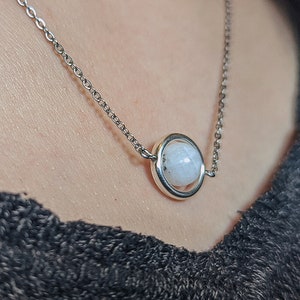 Könnte beinhalten: Eine silberne Kettenkette mit einem weißen Mondstein-Anhänger in einem silbernen Kreis.