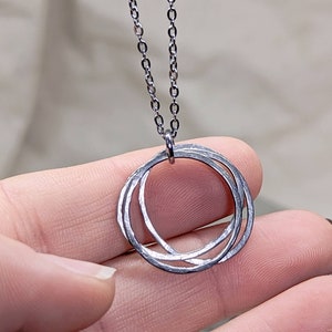 Può includere: Una collana d'argento con un ciondolo fatto di tre cerchi intrecciati.